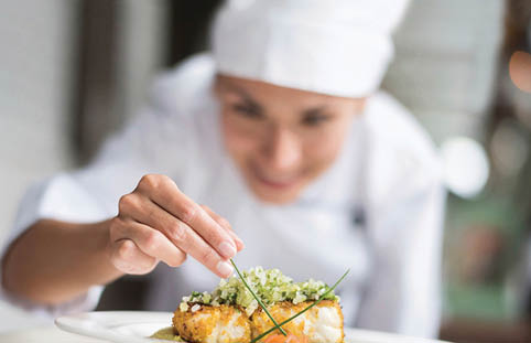 Cook decorating a plate and putting the ultimate touches - focus on foreground 
