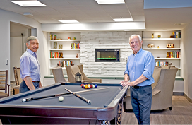 Two men standing in a living room, one on each side of a pool table. AI generated content