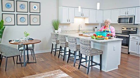 A woman is standing in a kitchen with a dining table and chairs. The table is set with fruit and a bowl. There is a microwave and oven in the kitchen. AI generated content