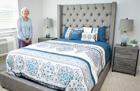 An elderly woman is standing in a bedroom with a large bed. AI generated content